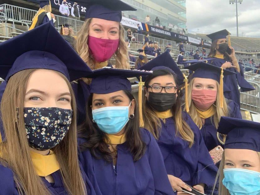 A group of graduates pose in caps, gowns, and masks