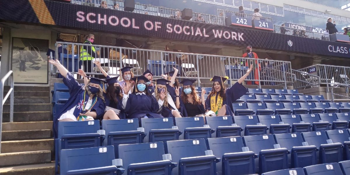 A group of graduates in caps and gowns celebrates in the stands of a stadium
