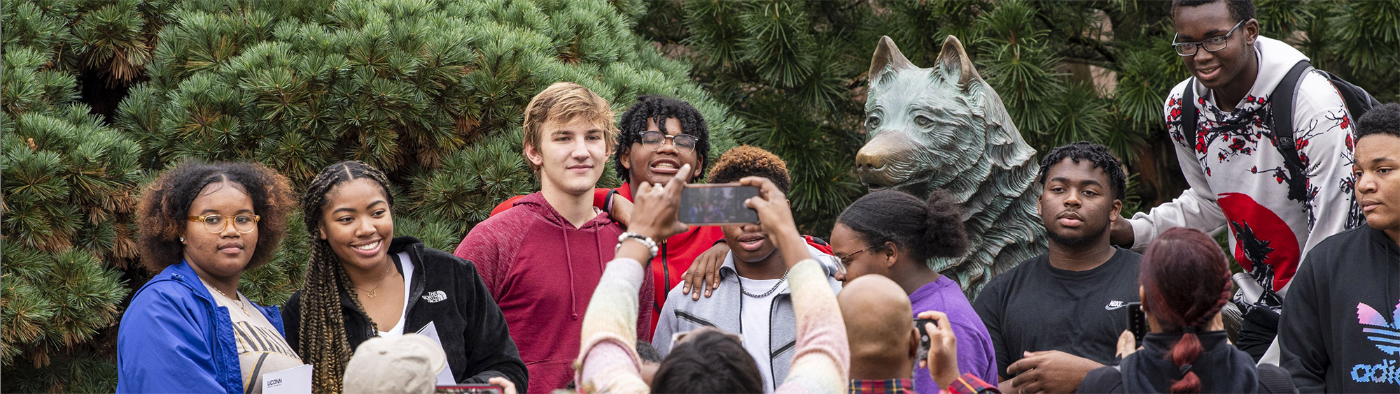 diverse group of prospective students posing for a picture in front of a jonathan the husky statue
